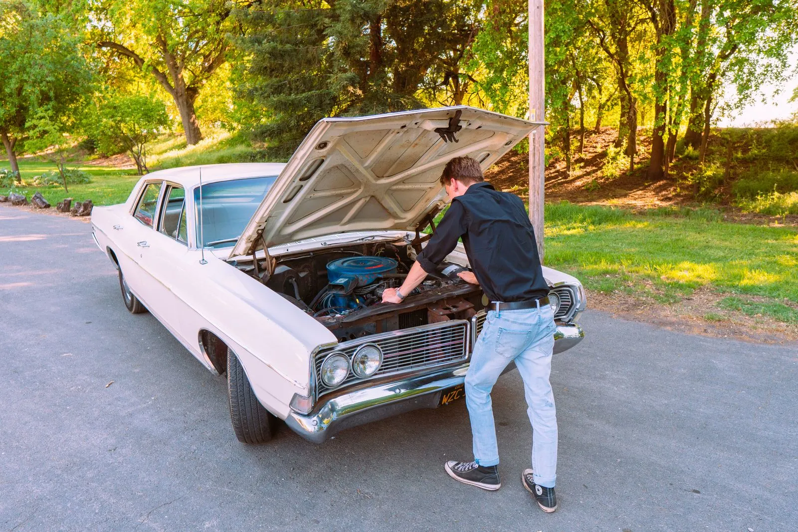 A man fixing a vintage car engine outdoors in Clarksburg, California, on a sunny day.